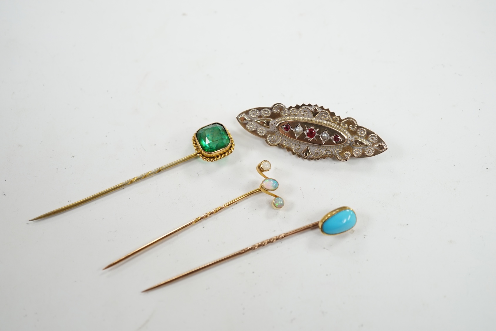 An Edwardian 9ct, ruby and seed pearl set cannetille work brooch, 46mm, together with three assorted gem set stick pins. Condition - fair